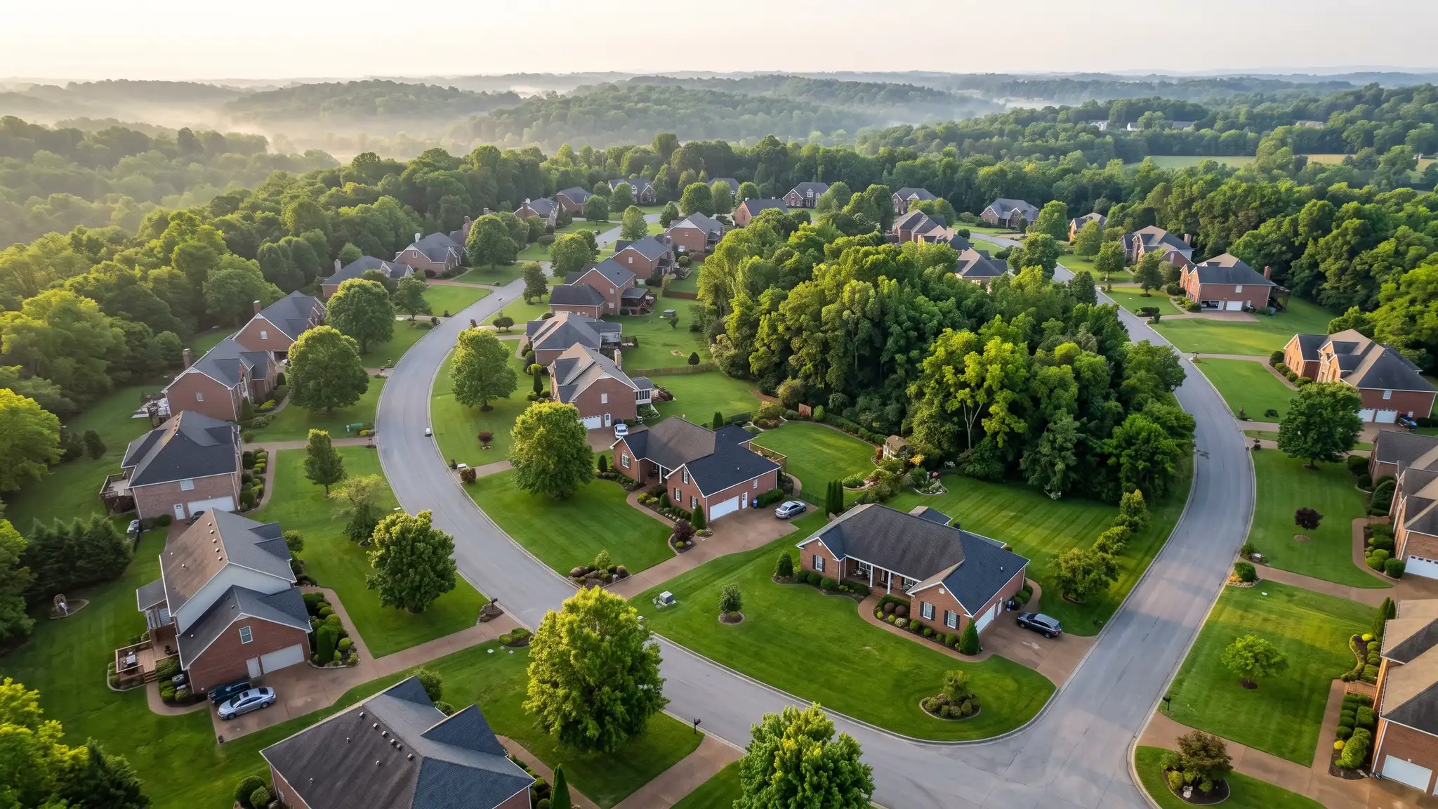 Landscaping FAQ | Music City Landscaper An aerial view of a Tennessee neighborhood with brick homes, mature trees and bright green landscaped lawns along winding streets in soft morning light